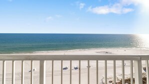 Udsigt til en strand fra en balkon med gelænder, sandstrand og hav.
