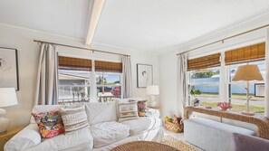 A bright living room with a white sofa, a wicker chair, and a view of the outside.