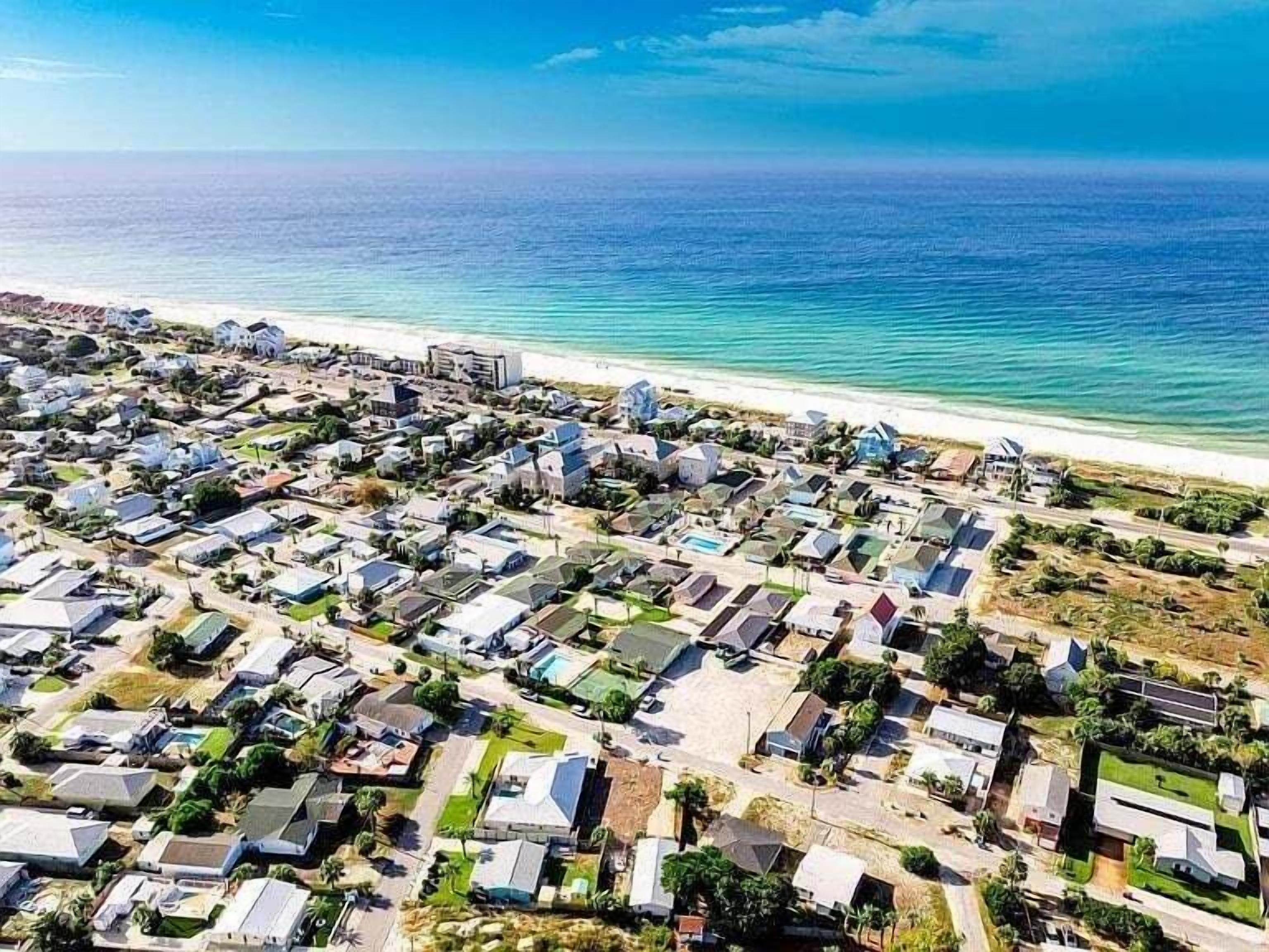 An aerial view of a coastal residential area with houses, roads, and a beach.