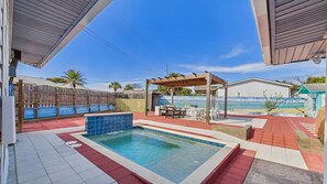 A pool area with a wooden pergola, outdoor furniture, and a fenced patio.