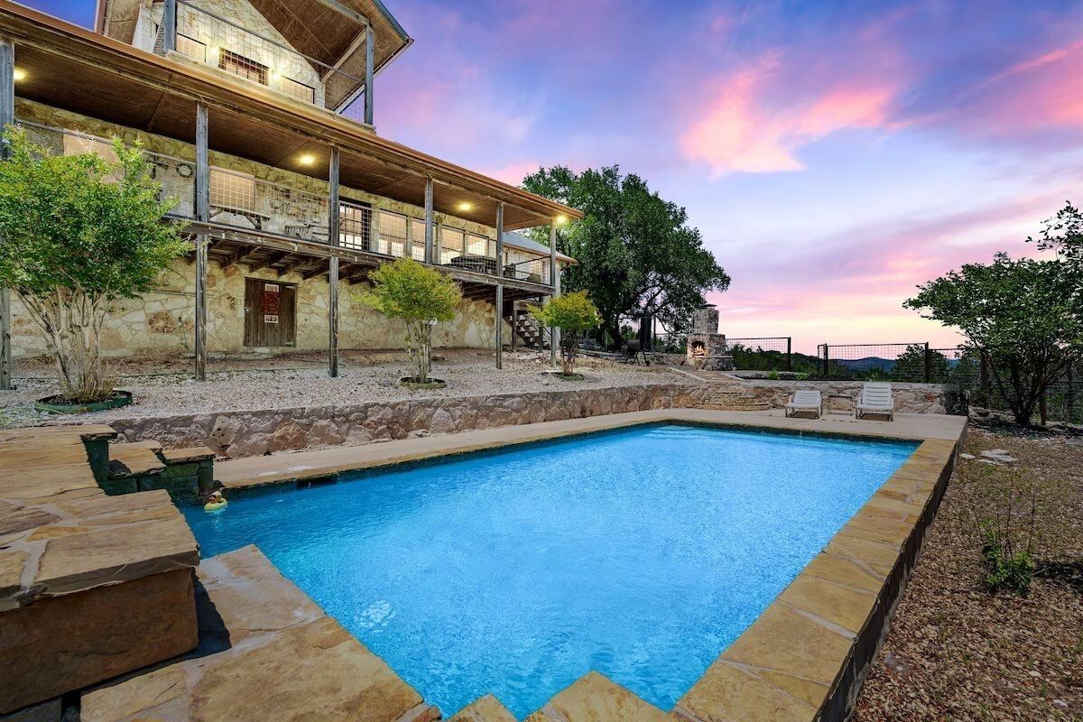 A swimming pool with stone edging, a wooden deck, and a stone building with a balcony.
