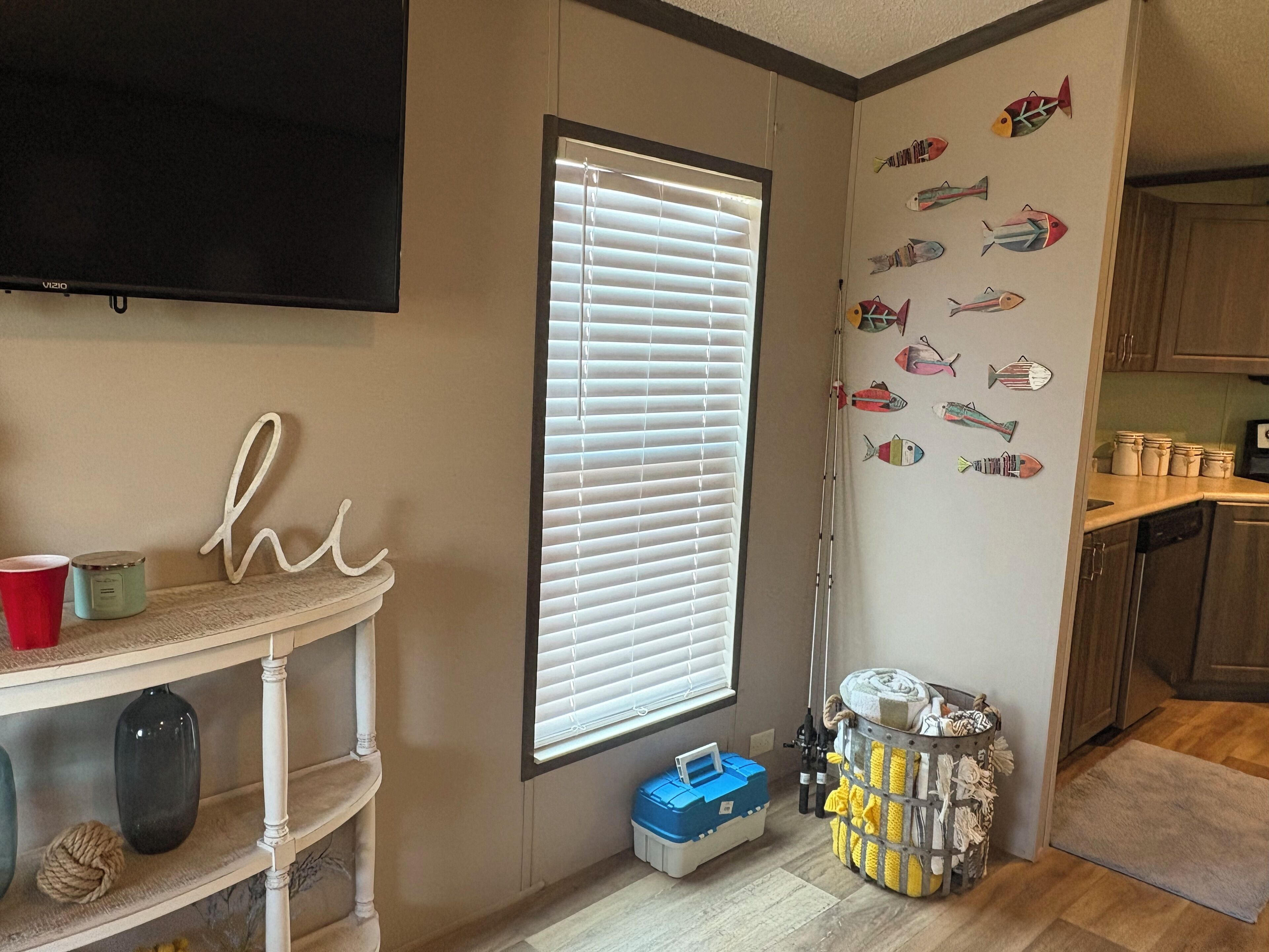 A kitchen with wooden cabinets, a window with blinds, a television mounted above the window, and a wall with fish decals.