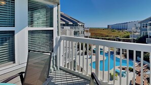 Een balkon met uitzicht op een zwembad, witte reling en een heldere lucht.