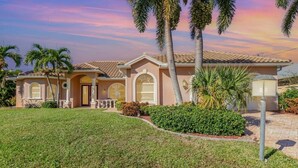 A two-story house with a tiled roof, a front porch, and palm trees. - Rose Lake Escape - Gulf Access & Pet Friendly (Cape Coral)