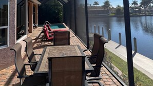 A covered patio with a pool, chairs, and a table. - Rose Lake Escape - Gulf Access & Pet Friendly (Cape Coral)