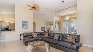 A spacious living room with a curved leather sofa, a coffee table, and a ceiling fan. - Rose Lake Escape - Gulf Access & Pet Friendly (Cape Coral)