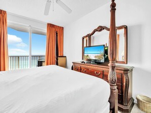 Ein Hotelzimmer mit einem großen Bett, einer Holzkommode, einem Fernseher und einem Balkon mit Vorhängen.