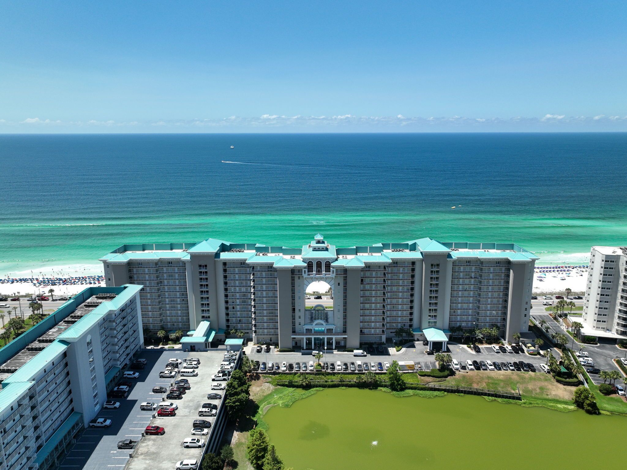 A large hotel with multiple floors, a parking lot, and a view of the ocean.