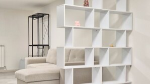 Ein modernes Wohnzimmer mit einer Eckcouch, einem weißen Regalsystem und einer schwarzen Metallkonstruktion.