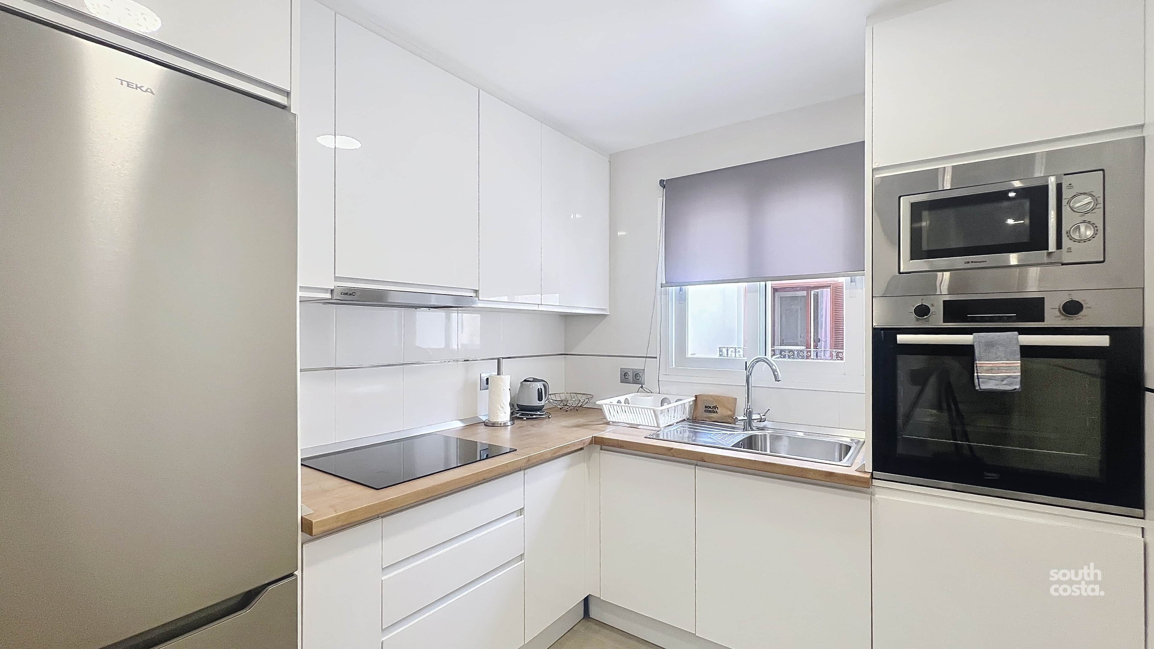A compact kitchen with white cabinets, a stainless steel refrigerator, a microwave, and an oven.