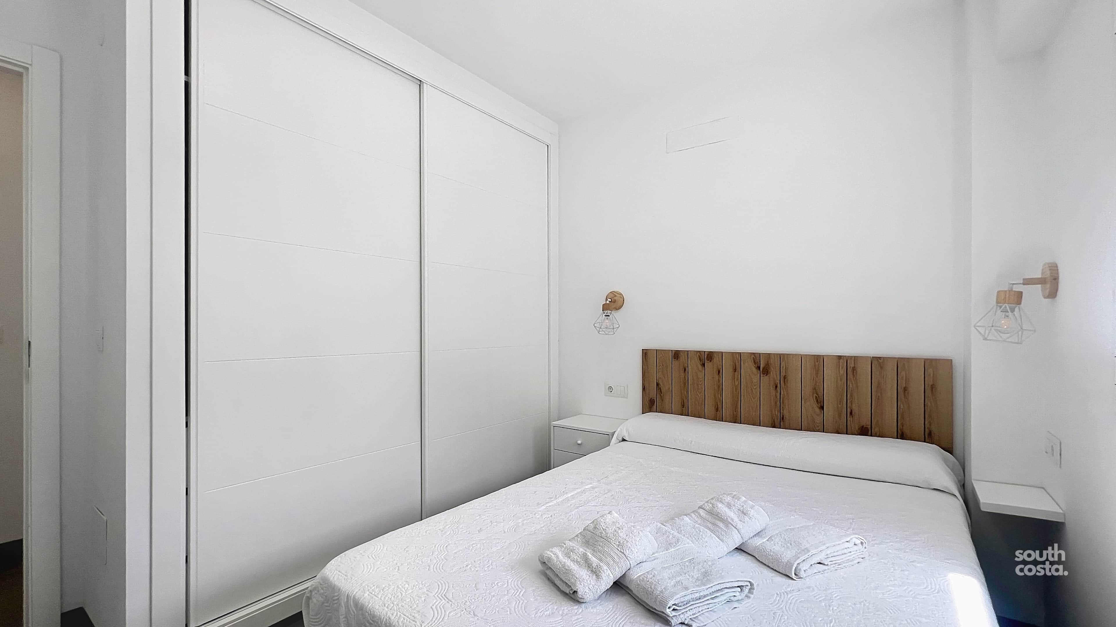 A bedroom with a bed, two bedside tables, a wooden headboard, and a wardrobe.