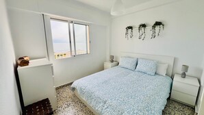 Un dormitorio con una cama, dos mesitas de noche, una ventana y vistas al mar.