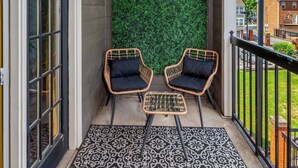 Ein Balkon mit zwei Korbstühlen, einem gemusterten Teppich und einer grünen Wand mit Blumen.