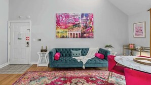 Ein Wohnzimmer mit einem türkisfarbenen Sofa, einem farbenfrohen Teppich und einem Stadtbild an der Wand.
