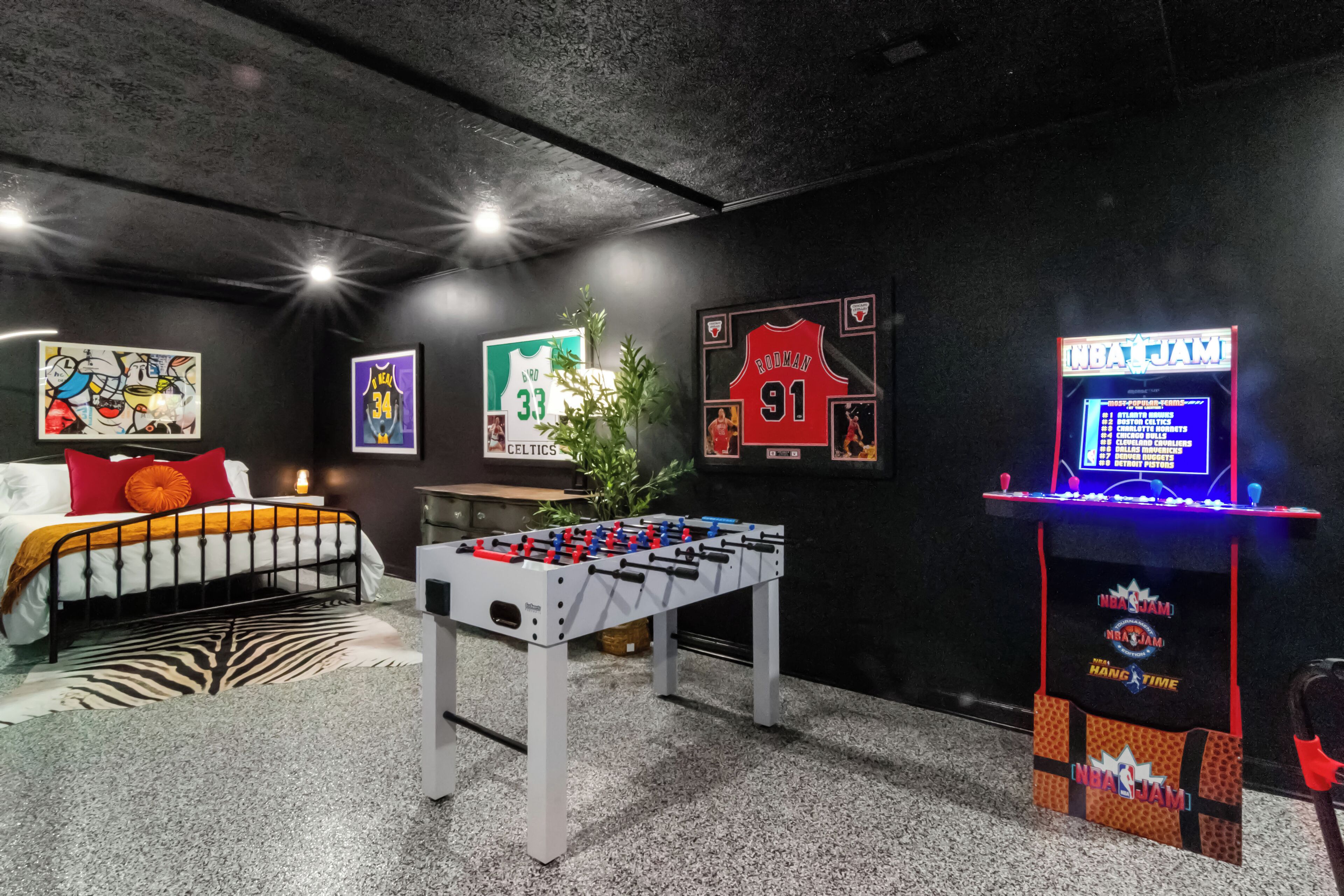 Een kamer met een tafelvoetbaltafel, een bed met een zebraprint vloerkleed en sportmemorabilia aan de muren.