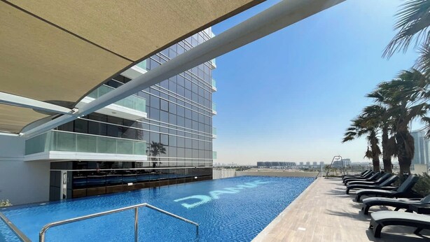 Un área de piscina moderna con vistas despejadas del horizonte de la ciudad, un solárium con baldosas y sillones de descanso.