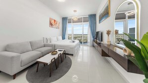 Una sala moderna con un sofá, una mesa de comedor y un televisor. Hay un ventanal con cortinas, una lámpara de techo y un espejo.
