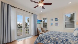 Un dormitorio con cama, ventilador de techo, televisor y vista al exterior.