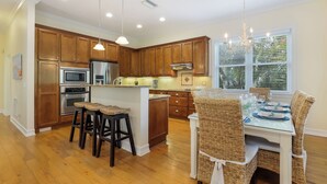 Una cocina con armarios de madera, electrodomésticos de acero inoxidable y un comedor con sillas de mimbre y una mesa de vidrio.