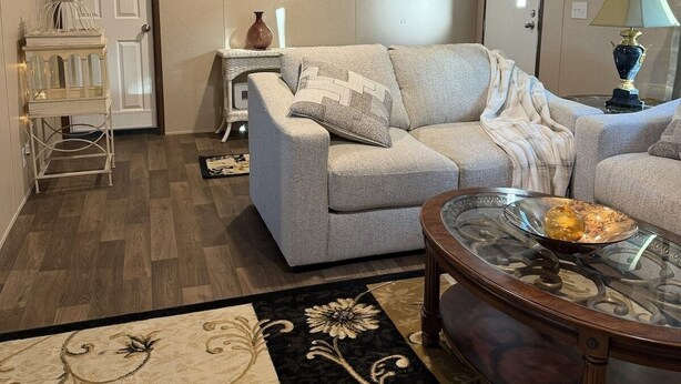Una sala de estar con un sofá gris, una mesa de centro de vidrio y una alfombra estampada.