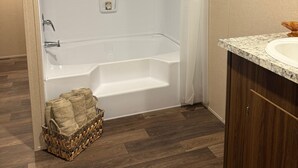 Un baño moderno con una bañera independiente, suelo de madera y encimera de mármol con un lavamanos.