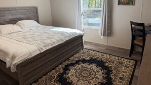 Un dormitorio con una cama grande, una ventana con cortinas, una silla y un cuadro en la pared.