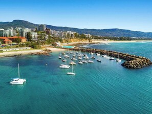 A coastal marina with multiple sailboats docked, surrounded by a rocky breakwater and a backdrop of residential buildings and hills. - Cityview Escape Poolside Living near CBD and Beach (Wollongong)