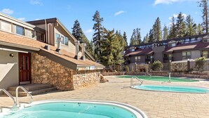 A pool area with two swimming pools, stone walls, and a building with a stone facade and a red door. - Cozy Mtn Retreat w/Fireplace | Mins to Village (Mammoth Lakes)