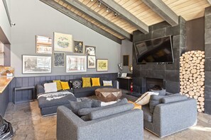 Ein modernes Wohnzimmer mit grauen Sofas, einem Holztisch und einem Kamin mit gestapelten Holzscheiten.