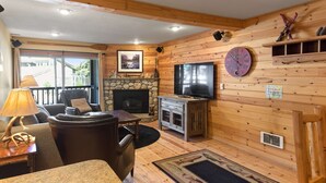 A cozy cabin interior with a fireplace, wooden walls, a television, and a large clock. - Cozy Mtn Retreat w/Fireplace | Mins to Village (Mammoth Lakes)