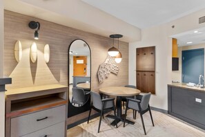 A modern hotel room with a wooden accent wall, a round dining table with chairs, a large mirror, and a pendant light. - Cozy Studio w King Bed, Fireplace & Kitchenette (Mammoth Lakes)