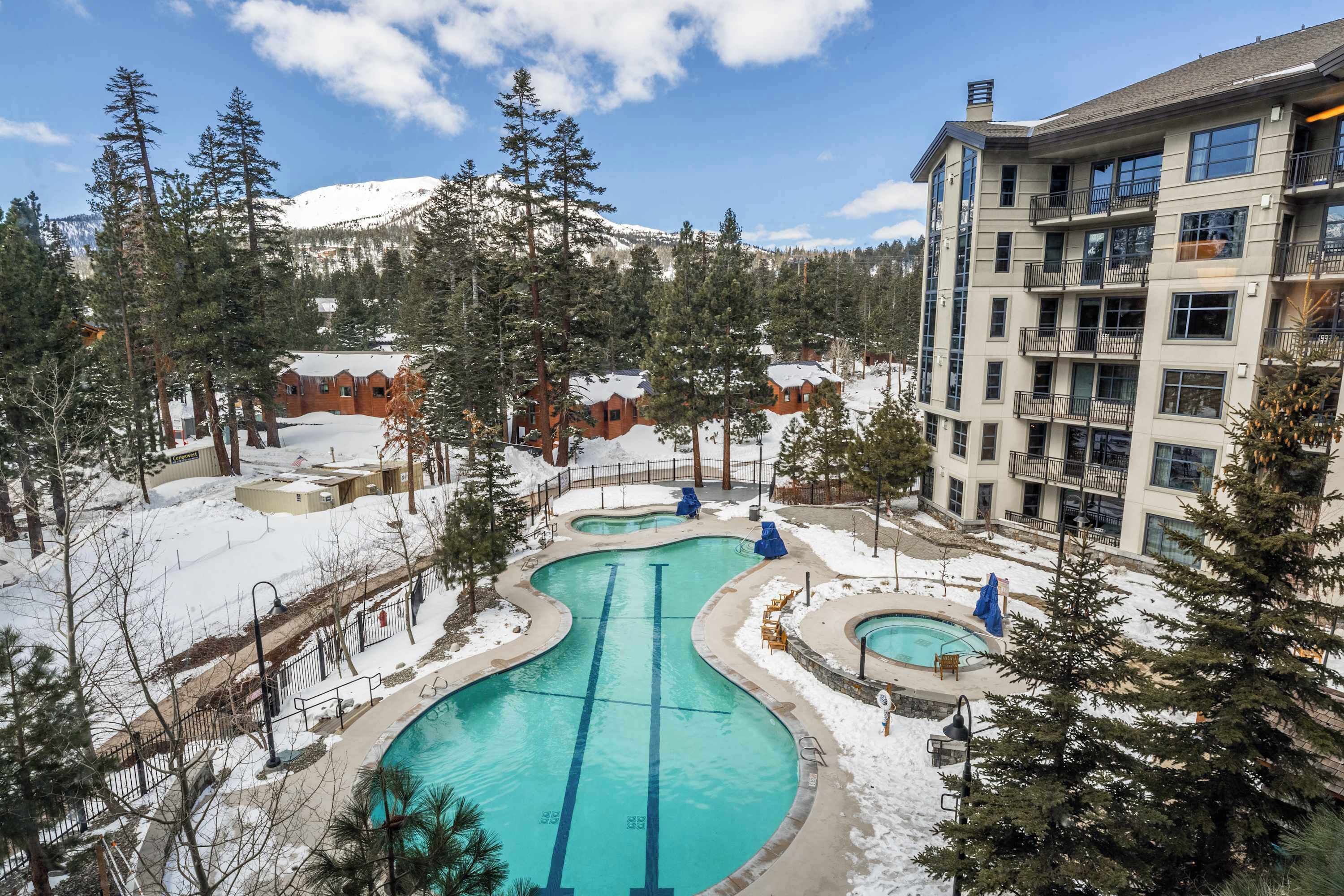A resort with a pool area, surrounded by snow-covered trees and a mountain in the background.