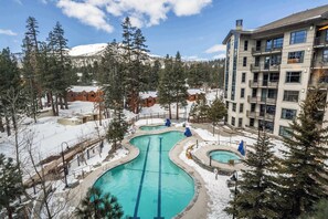 Un complexe hôtelier doté d’une piscine, entouré d’arbres couverts de neige et avec une montagne en toile de fond.