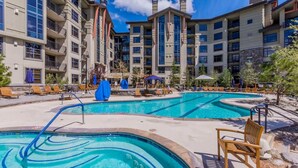 A hotel with multiple swimming pools, outdoor seating, and a clear sky.
