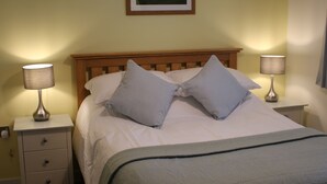 Cama bem arrumada com almofadas, mesa de cabeceira com abajur e um quadro na parede.