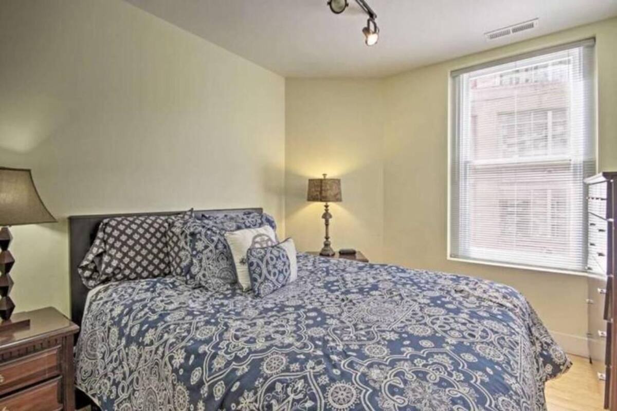 A bedroom with a bed, a nightstand, a lamp, and a window with blinds.