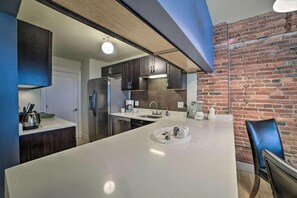 A modern kitchen with a large island, dark cabinets, and a brick wall. - Convention Center corporate apartments (Baltimore)