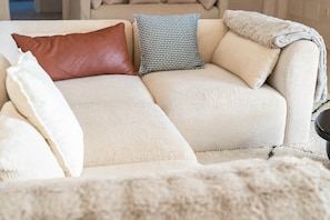 Ein beiges Sofa mit vielen Kissen, einer Decke und einem gemusterten Kopfkissen.