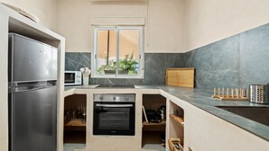 A compact kitchen with a refrigerator, oven, microwave, and a window with a view of greenery. - Casa Angeles, Frontline Beach House (Torreguadiaro)