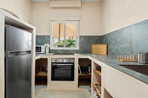 A compact kitchen with a refrigerator, oven, microwave, and a window with a view of greenery. - Casa Angeles, Frontline Beach House (Torreguadiaro)