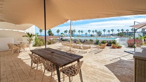 An outdoor patio with a wooden table and chairs, a pool in the background, and palm trees. - Casa Angeles, Frontline Beach House (Torreguadiaro)