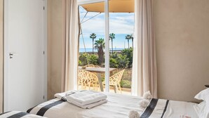 Ein Hotelzimmer mit Bett, einem Fenster mit Vorhängen und Blick auf Palmen und das Meer.