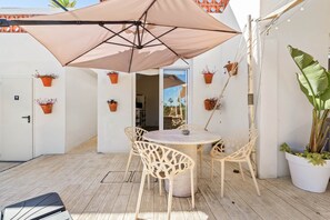 Una terrazza con un tavolo rotondo e sedie, un ombrellone grande e piante in vaso.