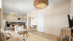 A modern living room with a sofa, coffee table, and a TV stand. A kitchen is visible in the background with a dining area. - Casa Ibrahim, Frontline Beach House (Torreguadiaro)