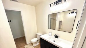 Un baño con inodoro blanco, tocador negro con espejo y lavabo blanco.