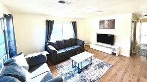 Una sala de estar con sofá, una mesa de centro, televisor y ventana con cortinas.