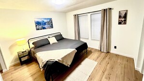 Un dormitorio con cama, mesita de noche, lámpara y ventana con cortinas.