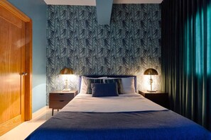 Une chambre à coucher avec un papier peint à motifs, un lit avec des oreillers, deux lampes de chevet et une porte en bois.