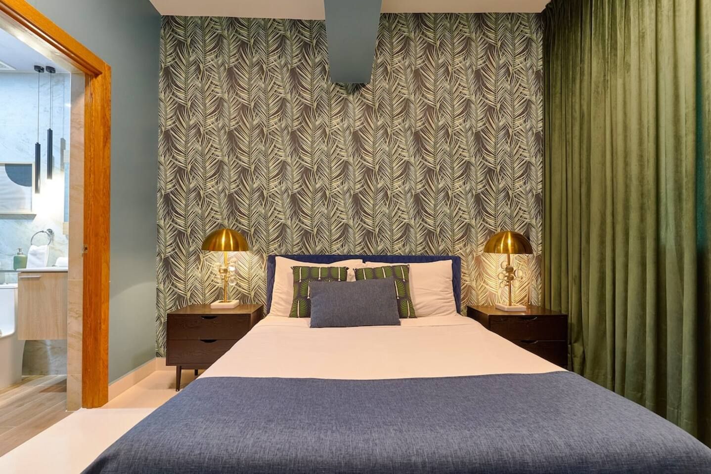Une chambre d’hôtel avec un lit, deux lampes de chevet, un papier peint à motifs et un rideau vert.
