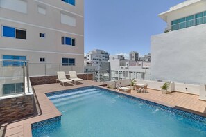 Une piscine sur le toit, dotée de chaises longues et offrant une vue sur le paysage urbain.